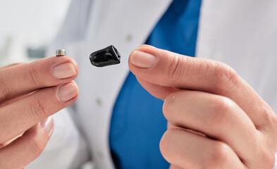 Hearing aid battery replacement. Hearing specialist showing ITE hearing aid and battery for it, holding them in her hands in front of him, close-up
