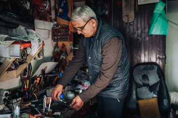 Fototapeta na wymiar An old cobbler is gluing shoe sole and repairing footwear at workshop.