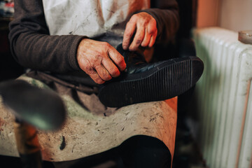 Close up of a senior artisan holding a boot his hands and repairing it.