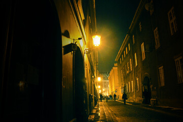 Night cityscape of Poznań, alley with tenement houses lit by lanterns, yellow light