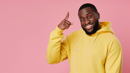 Fototapeta premium Cheerful Man in Yellow Hoodie Pointing to Head on Pink Background