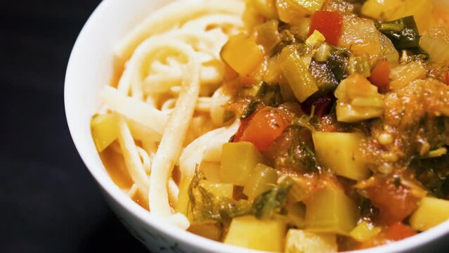 Stewed vegetables with meat and noodles in a bowl. Lagman. Black background.
