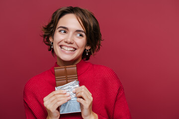 Young happy woman in red sweater holding chocolate bar and looking away