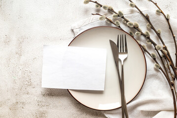 Easter table setting with empty white plate, white blank paper card and spring willow branches on...