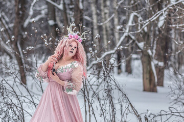 A beautiful spring fairy, a dryad with deer antlers and a crown and a light pink dress in a snowy forest.A fabulous photo. The concept of changing seasons.
