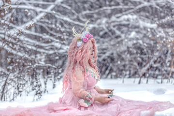 A beautiful spring fairy, a dryad with deer antlers and a crown and a light pink dress in a snowy forest.A fabulous photo. The concept of changing seasons.