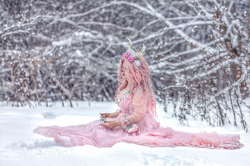 A beautiful spring fairy, a dryad with deer antlers and a crown and a light pink dress in a snowy...