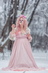 Fototapeta na wymiar A beautiful spring fairy, a dryad with deer antlers and a crown and a light pink dress in a snowy forest.A fabulous photo. The concept of changing seasons.