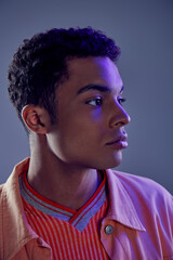 Obraz premium portrait of handsome african american guy in peach shirt looking away on grey with blue light
