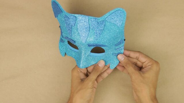 Hands gluing last details, blue diamond foam Catboy mask from PJ Masks for carnival