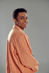 happy man in peach shirt standing against grey wall, showcasing his impeccable fashion sense