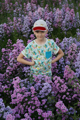 Summer stylish look for child, fashionable kid, cute boy and purple flowers. Street style. Lilac, violet flowers in floral garden, field. Cute child, summer blossom, spring bloom