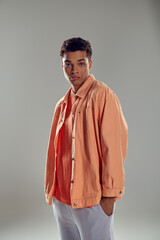 stylish man in peach shirt standing against grey wall, showcasing his impeccable fashion sense