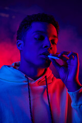 african american man holding rolled cigarette while standing on dark blue background with red light