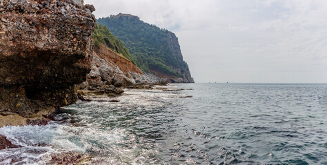 Panoramic view of the rocky coast, the silhouette of a fisherman with a fishing rod and three boats in the distance sailing along the Mediterranean Sea in the city of Alanya, Turkey.