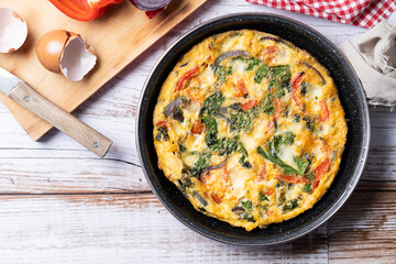 Italian Frittata made with spinach, tomatoes, onion and peppers on white wooden table. Top view