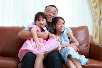 Grandfather and two cute little granddaughter's sitting on the sofa in the house, smiling, laughing, talking and having fun. happy time Love and warmth. Asian family concept