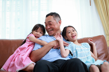 Grandfather and two cute little granddaughter's sitting on the sofa in the house, smiling, laughing, talking and having fun. happy time Love and warmth. Asian family concept