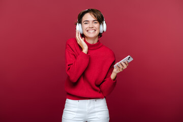 Naklejka premium Smiling happy young woman wearing red turtleneck, listening to music in headphones