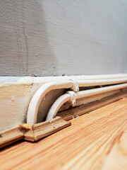 Two white water pipes attached on wooden skirting by floor of a room. Poor quality job. Poor old...