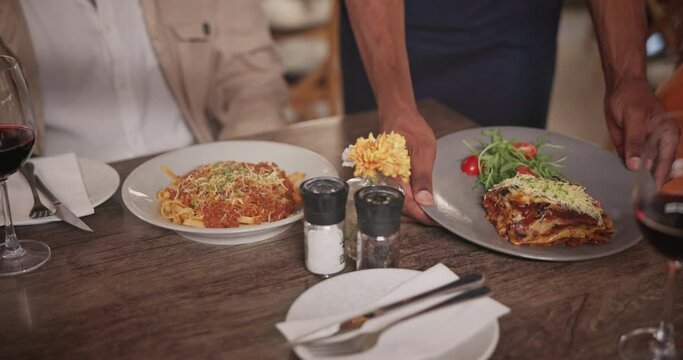 Waiter, restaurant and hands with food, people and woman at table on date Italian cuisine with wine. Closeup, lasagne at fancy bistro with spaghetti, pasta and table for dinner or lunch service