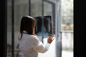 Female doctor examining a chest X-ray film with attention in a modern clinic setting.