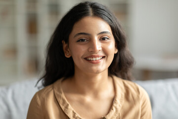 Portrait of young indian woman resting at home, joyful lady sitting on comfortable sofa and smiling...