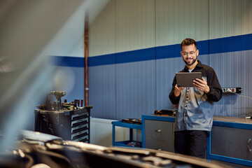 A smiling auto mechanic working at his garage, using a digital tablet.