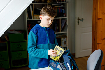 School kid boy getting ready in the morning for school. Healthy child filling satchel with books,...