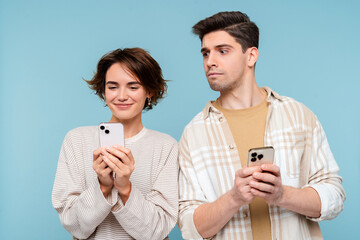 Interested man looking at smartphone of his girlfriend isolated on blue background