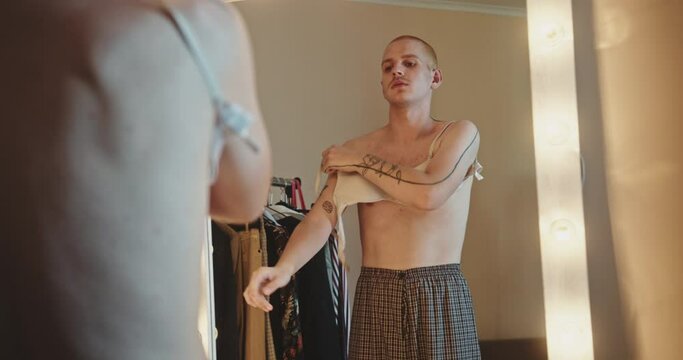 Homosexual person putting on bra in front of mirror