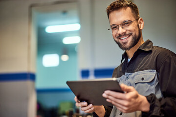 A portrait of a smiling mechanic man, dressed in a uniform, using a digital tablet. - obrazy, fototapety, plakaty