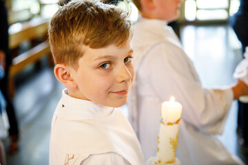 Little kid boy receiving his first holy communion. Happy child holding Christening candle....