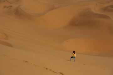 Fototapeta na wymiar Distant view of woman that is walking in the sands of Namibia, Africa desert