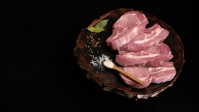 Raw fresh pork meat cut into pieces for frying (pork steak) rotating on a kraft wooden board on a black background. Top view. Space for caption