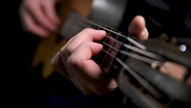 Playing an acoustic guitar on a black background. The musician clamps the frets of the guitar on the neck. Musical instrument in male hands. Close-up. Soft focus.