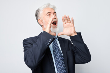 Portrait of senior businessman in suit shouting loudly with hands, news, palms folded like megaphone isolated on white background.