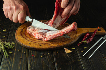 A butcher uses a knife to separate meat from the bone on a kitchen board before preparing dinner or...