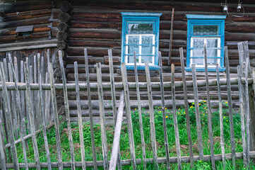 A stockade in the village. A fence in the village. A wooden village house is visible behind the fence. An old wooden house in the village.