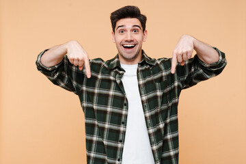 Portrait of excited amazed man keeps mouth opened, being astonished, pointing fingers down