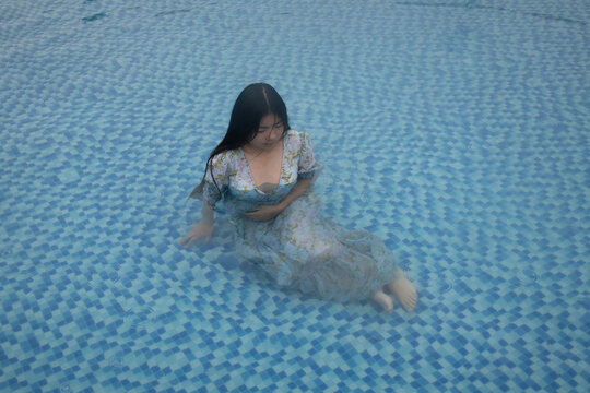 woman sitting water in swimming pool wearing light blue dress