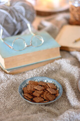 Cup of tea or coffee, cookies, books, glasses, e-reader, almonds, ball of yarn, knitting needles and lit candles on the table. Hygge at home. Selective focus.