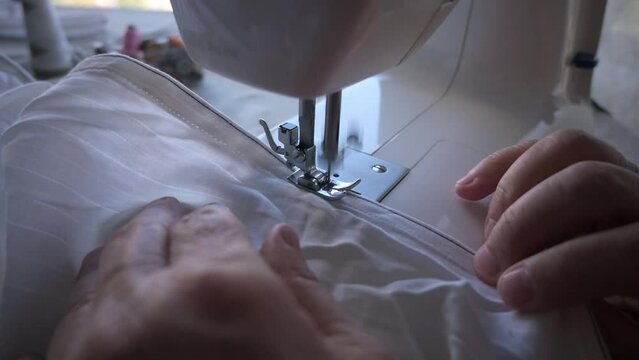 Elderly hands sew fabric behind the machine. A needle and thread stitches fabric close-up.
