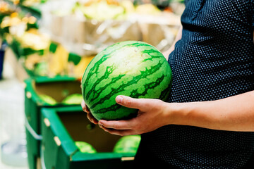 Hand is holding watermelon from supermarket shelf, close up photo