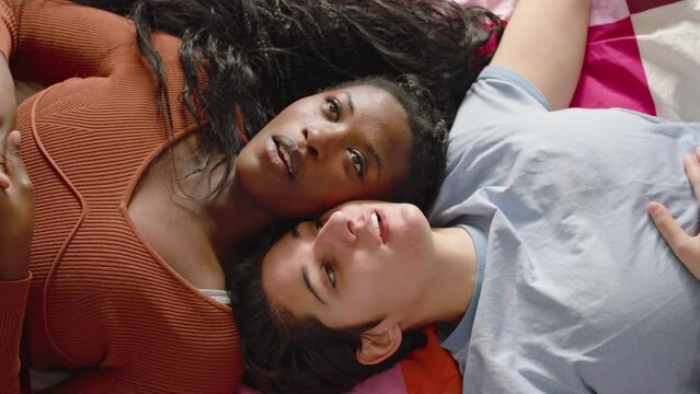 In the bedroom, portrait of  a couple of multi-ethnic girls hug and cuddle.
The two cute lesbian girls lying on the bed talking and having fun together.
Concept of diversity, love, and valentine's day