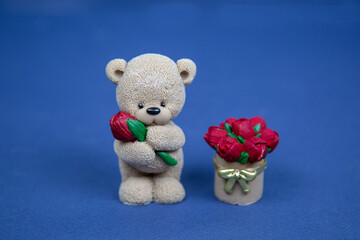 Sweets in the form of a gray bear with a flower and a basket of red roses on a blue background.  Confectionery drinks tea coffee.