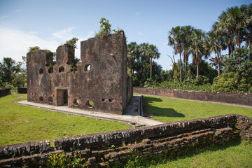 An ancient brick fortress with gun loopholes on a clear sunny day against a background of palm trees and blue sky, Fort Zealand, Guyana. Medieval architecture, world tourism.