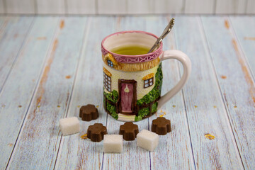 A ceramic mug with a handle depicting the windows of a wooden house, sugar and sweets on a gray wooden table. Design, painting, applied art, ceramics.