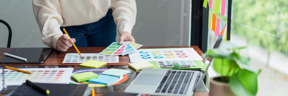 Poster creative graphic designer holding color sample and comparing color swatch on document to designing