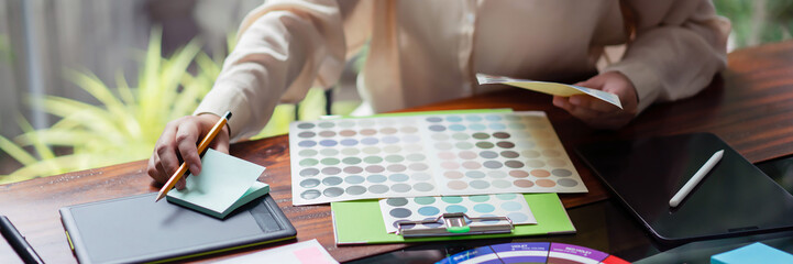 Creative graphic designer choosing color on color swatch and writing notes idea in adhesive note